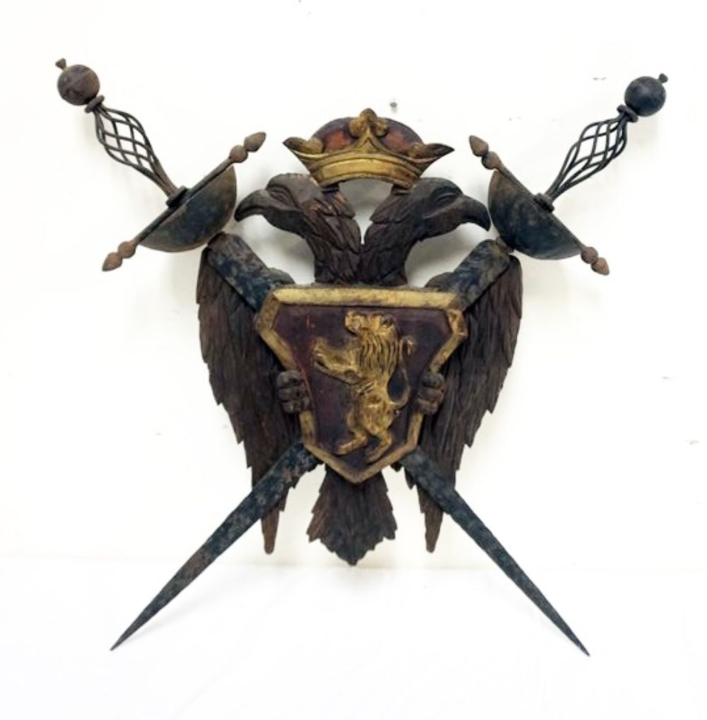 CARVED ARMORIAL COAT OF ARMS: WOOD CARVED ARMORIAL COAT OF ARMS WITH METAL CROSSED SWORDS, APPROXIMATELY 25 IN HIGH X 24 I WIDE