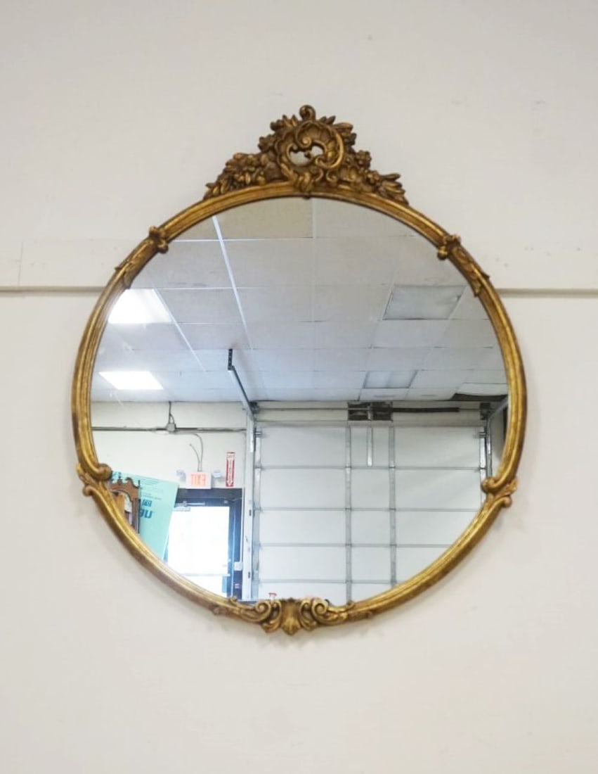 ORNATE GILT EDGE ROUND HANGING MIRROR: ORNATE GILT EDGE ROUND HANGING MIRROR WITH SCROLLED FLORAL CREST, APPROXIMATELY 30 IN X 36 IN