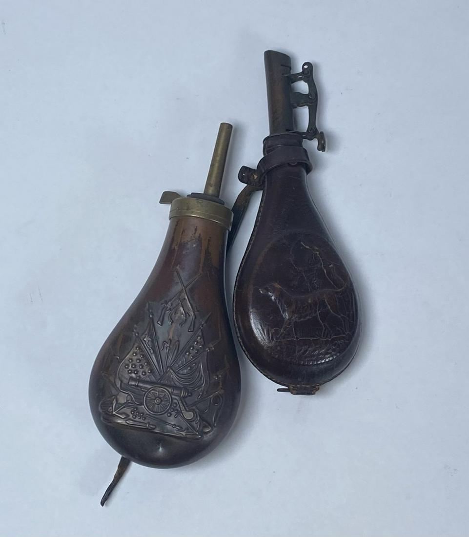 PAIR - CIVIL WAR ERA GUN POWDER FLASKS: ONE METAL FLASK WITH DESIGNS OF CANNON, FLAGS, RIFLES, SWORDS AND ONE LEATHER WITH DESIGNS OF HUNTING DOGS AND TREES.