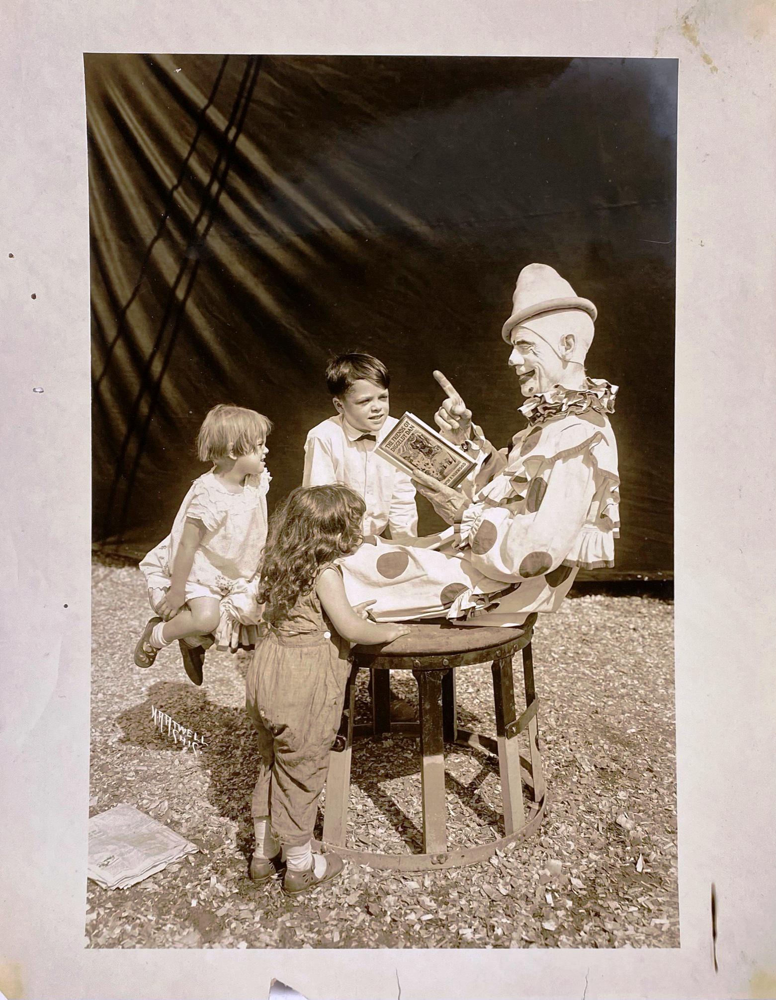 H.A. ATWELL PHOTOGRAPH OF CLOWN WITH CHILDREN: H.A. ATWELL PHOTOGRAPH OF CLOWN ATOP AN ELEPHANT TUB READING "THE FRIENDS OF DIGGELDY DAN" TO THREE CHILDREN. 11"X14"