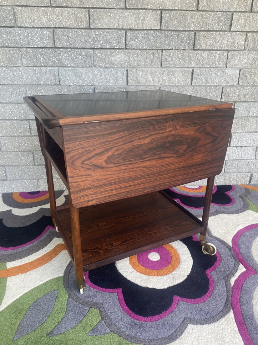 LUDWIG PONTOPPIDAN SERVING CART: ROSEWOOD, BLACK LAMINATE TOP. 27L, 20W, 28H. HAVING A PAIR OF 10.5" DROP LEAVES.