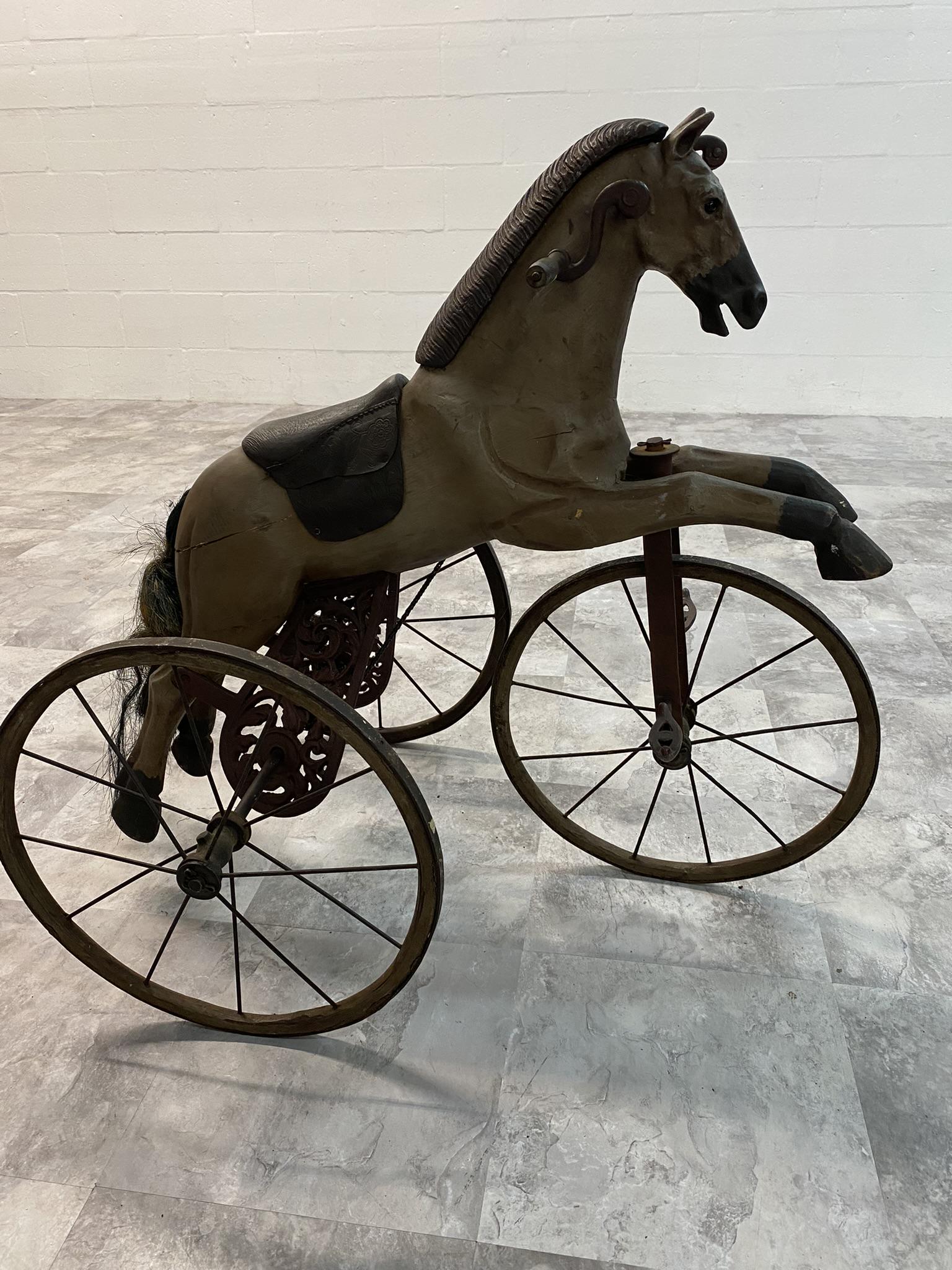 HORSE VELOCIPEDE PEDAL TOY: HORSE VELOCIPEDE PEDAL TOY. EARLY FORM WITH HAND CRANKS AND FLORAL CAST IRON SUPPORTS. AND CARVED HORSE WITH GLASS EYES. LEATHER SADDLE, WOODEN HUBS. HORSE HAIR TAIL REPLACED. A VERY EARLY HORSE TOY F