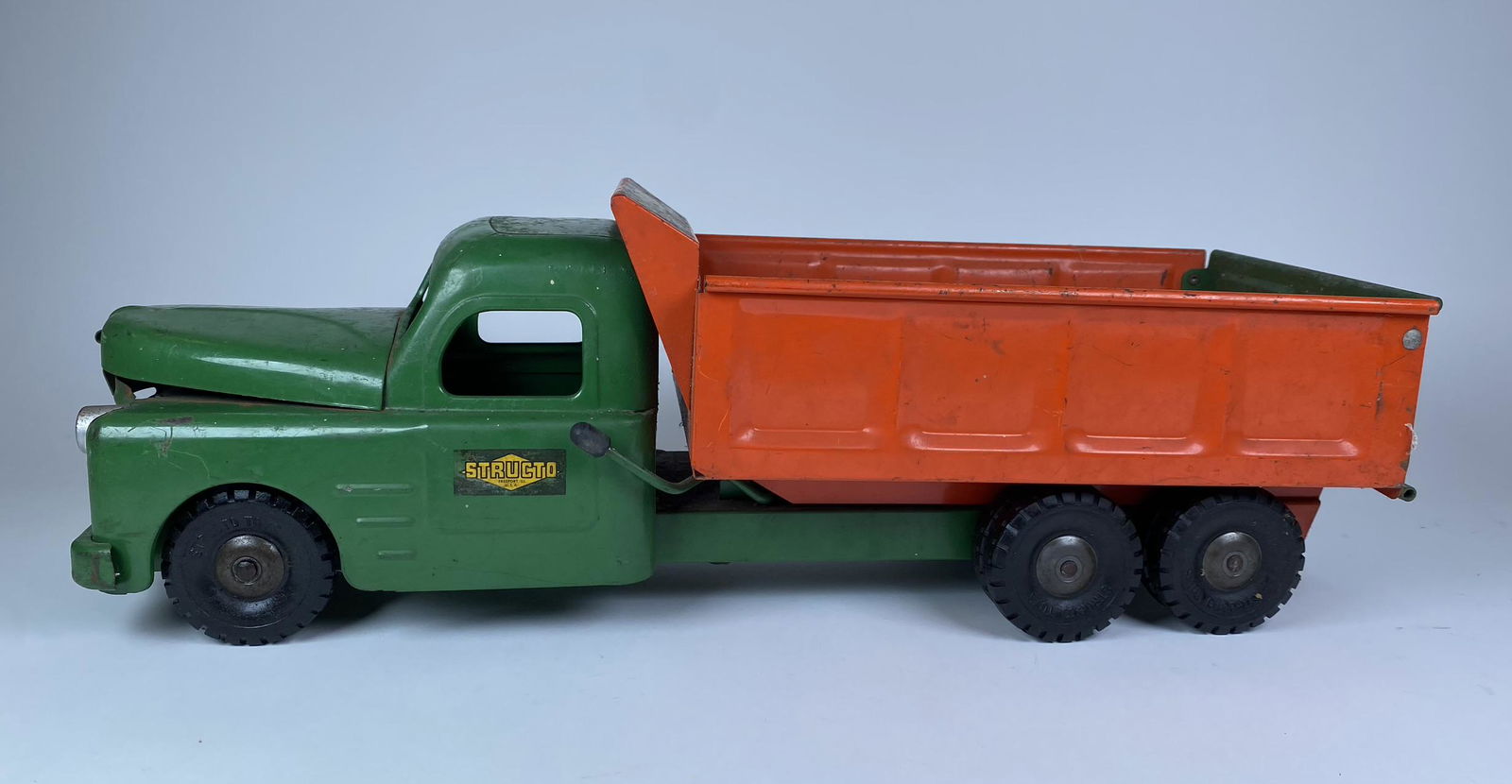 STRUCTO HYDRULIC DUMP TRUCK: STRUCTO HYDRULIC DUMP TRUCK. GREAT GREEN AND ORANGE COLOR AND GOOD STICKERS. ENGINE BAY OPENS AND PLASTIC ENGINE PRESENT. WORKING TAILGATE AND HYDRAULIC LIFT. 21" L