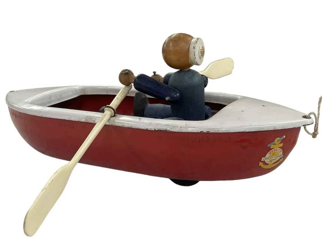 WOODETTE COAST GUARD PULL TOY: MINOR PLAY WEAR. ORIGINAL PULL KNOB AND STRING, ARTICULATING WOODEN SAILOR WITH TIN ROWBOAT ACTION. 12"L