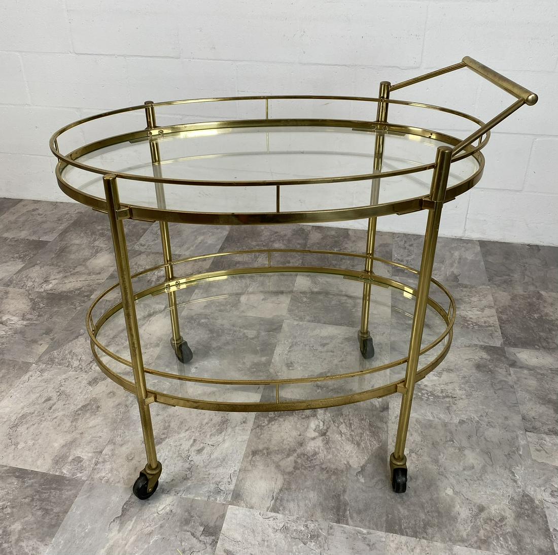 BRASS TEA CART: AN OVAL TIERED BRASS ROLLING TEA CART HAVING GLASS SHELVES. SCATTERED WEAR AMONG ALL METAL PARTS. 31"X18"X30"
