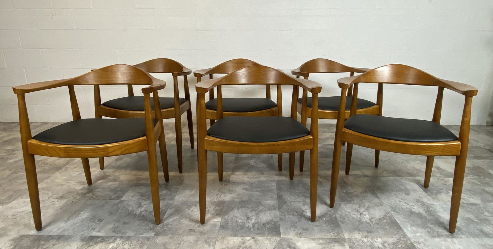 AFTER HANS WEGNER THE CHAIR: GROUPING OF 6 CHAIRS IN THE MANNER OF HANS WEGNER. BLACK UPHOLSTERY WITH OAK STRUCTURE. NO LABEL. MINOR WEAR. 24"W, SEAT 19", BACK 30", 20"D