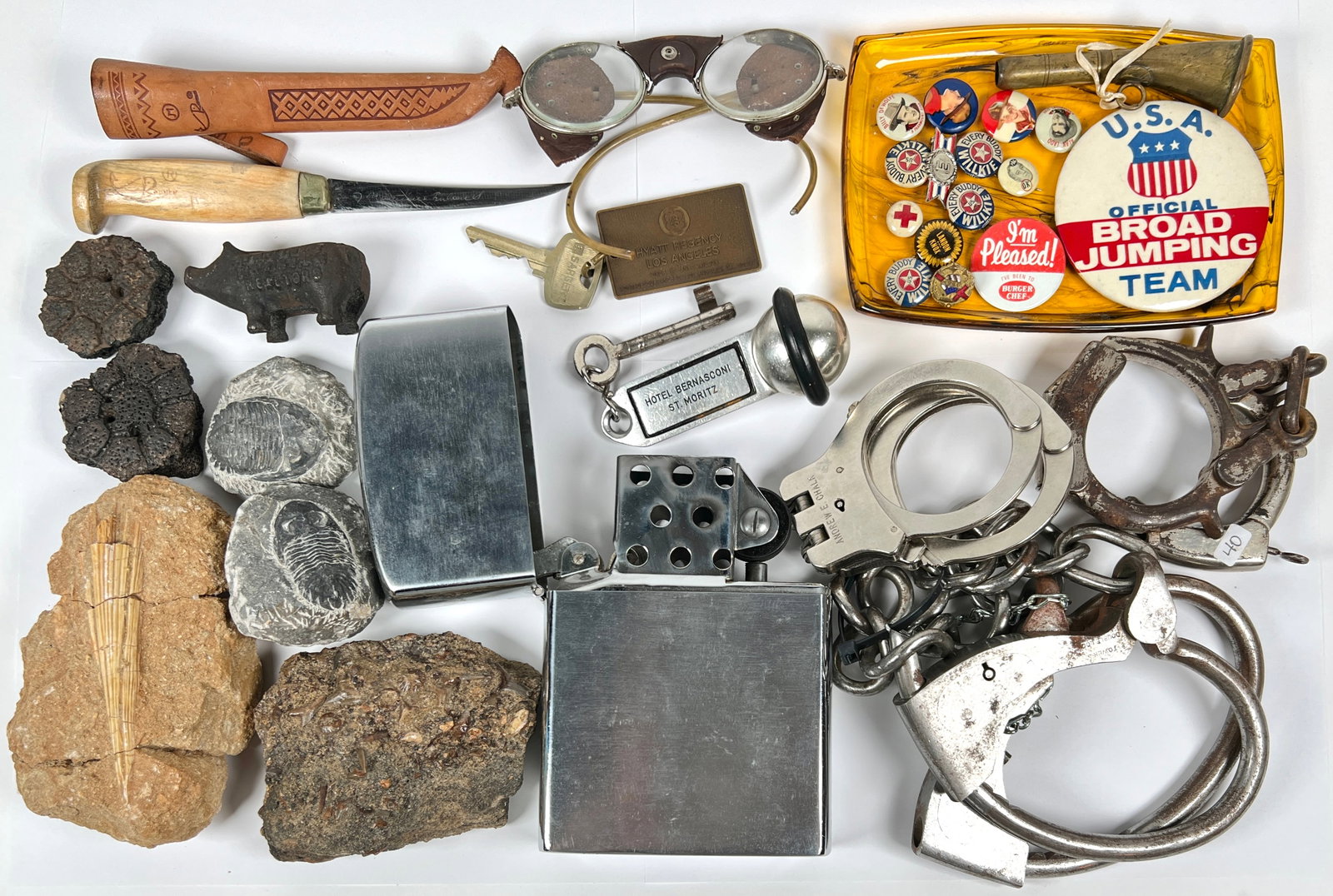 GENTLEMAN'S JUNK DRAWER: JUNK DRAWER FINDINGS INCLUDING HAND-CUFFS, SHACKLES, OVERSIZED LIGHTER, FOSSILS, HOTEL KEYS AND MORE