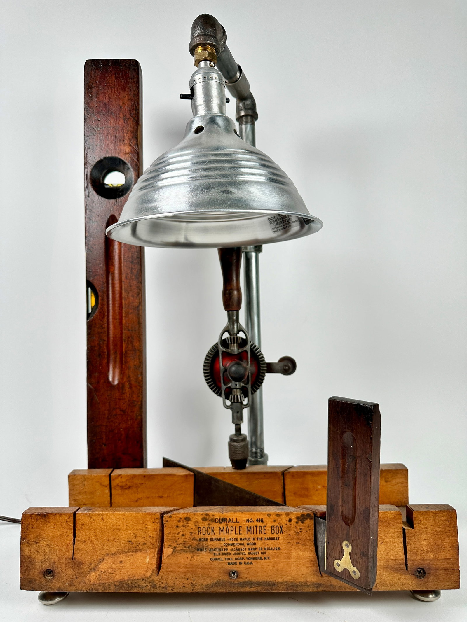 FOLK ART CARPENTRY LAMP: ASSEMBLED FROM CARPENTER'S TOOLS, MITRE BOX, SQUARE, RULER, HAND DRILL. WORKING CONDITION. 23"H