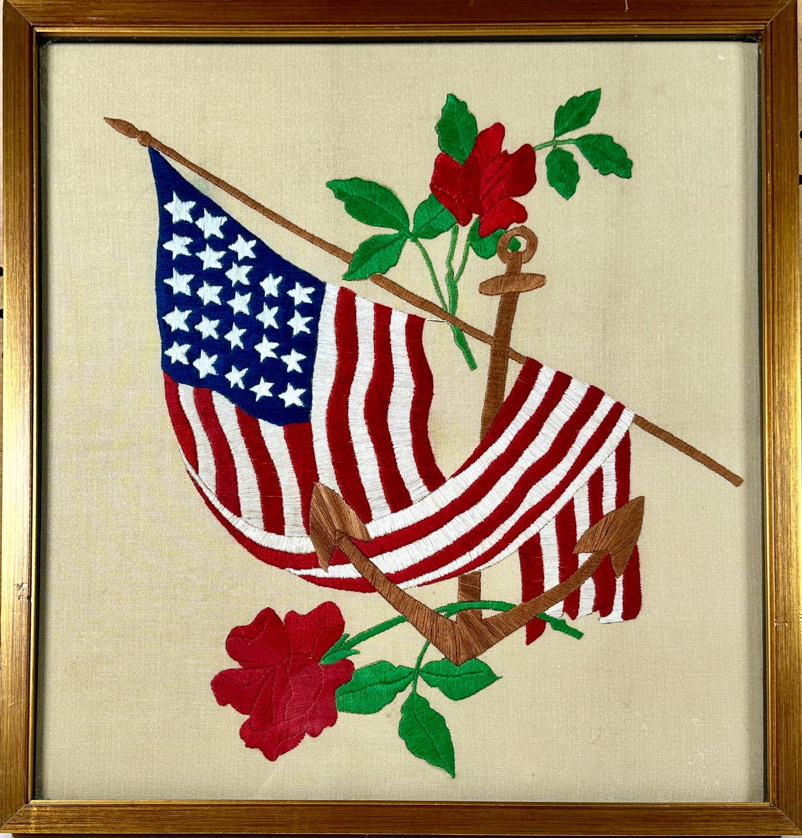 AMERICANA HAND-STITCHED FABRIC: HAND-STITCHED UNITED STATES FLAG DRAPED OVER AN ANCHOR WITH ADORNING ROSES. FRAMED, 18"X19"