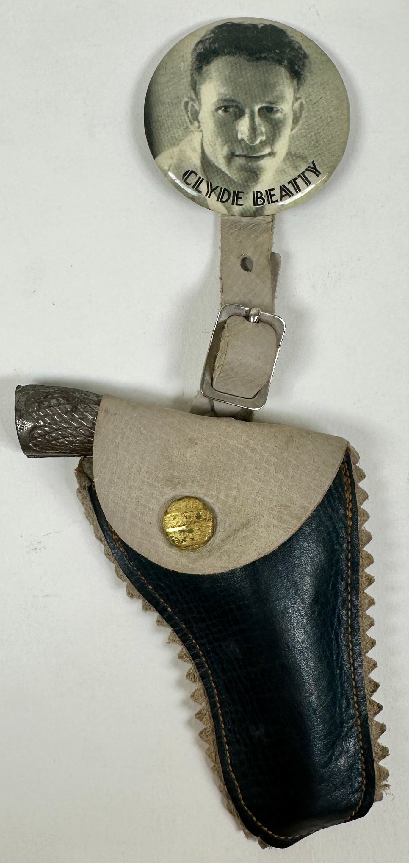 CLYDE BEATTY SOUVENIR: CLYDE BEATTY SOUVENIR PIN BACK BUTTON WITH GUN IN HOLSTER FOB. BUTTON IS 1.75"