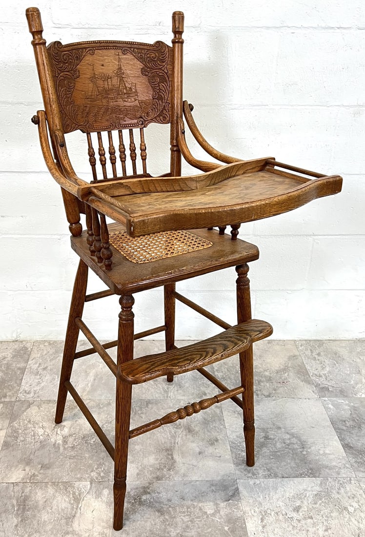 U.S.S. MAINE BATTLESHIP - CHILDREN'S HIGH CHAIR: CARVED BACK BEARING AN IMAGE OF THE U.S.S. MAINE BATTLESHIP. THE U.S.S. MAINE WAS A SECOND CLASS BATTLESHIP THAT EXPLODED AND SANK IN HAVANA HARBOR ON FEBRUARY 15, 1898, KILLING 266 CREW MEMBERS, A PI