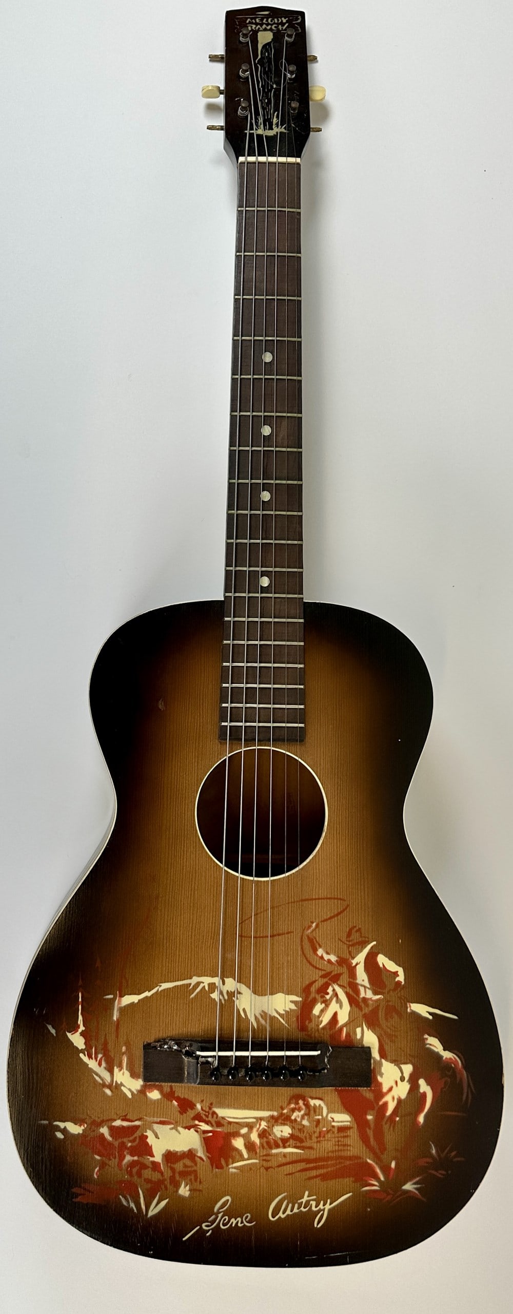 MELODY RANCH - GENE AUTRY GUITAR: VINTAGE GENE AUTRY JUVENILE GUITAR. OVERALL GOOD, MISSING A COUPLE OF TUNING THUMB SCREWS.