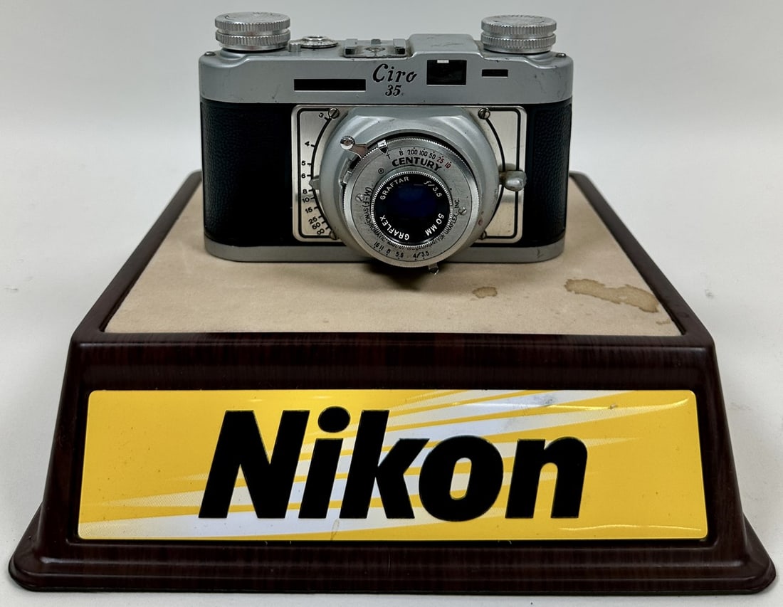 NIKON CAMERAS ADVERTISING DISPLAY: PLASTIC DISPLAY PLATFORM, INCLUDES GRAFLEX CIRO 35 CAMERA.