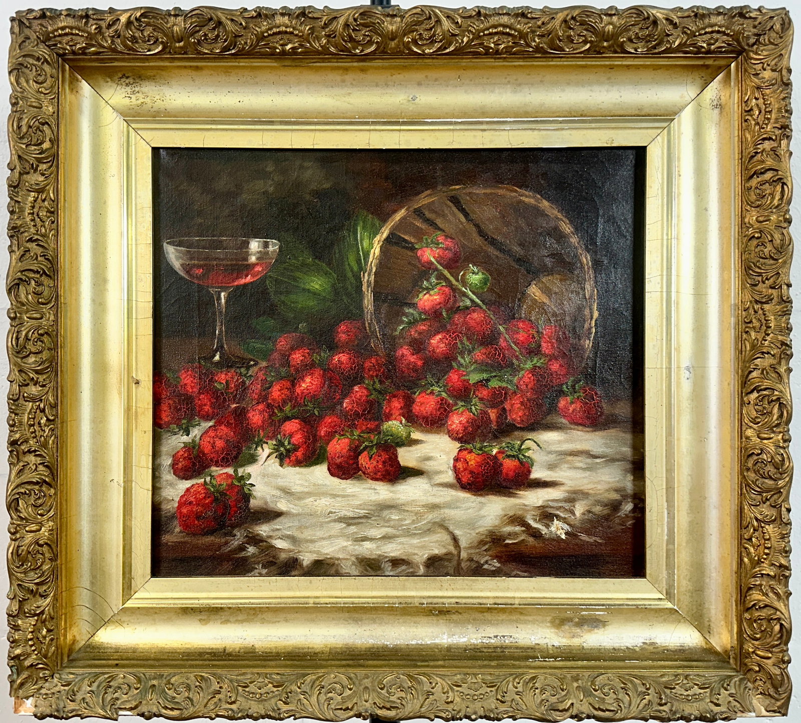 STRAWBERRIES STILL LIFE PAINTING: 19TH CENTURY UNSIGNED OIL ON CANVAS PAINTING OF STRAWBERRIES SCATTERED FROM BASKET AMONG A STEM OF WINE. CRAQUELURE THROUGHT, SMALL, REPAIRABLE PUNCTURE IN LOWER RIGHT, GILT GESSO FRAME WITH SCATTERED