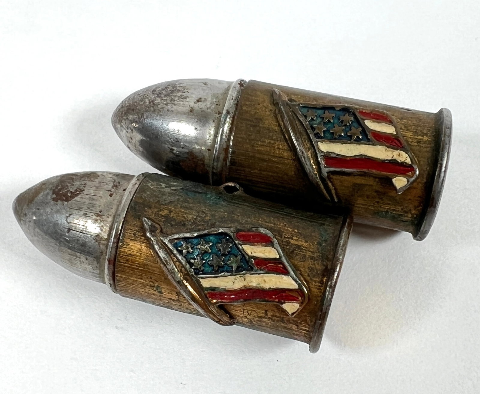 WWI ERA BULLET TRENCH ART PINS: PAIR OF U.S. FLAG ADORNED BULLETS, MISSING PINS ON VERSO. PROTECTED BY FLAG ENGRAVED ON CAP. EACH APPROX. 1.375"