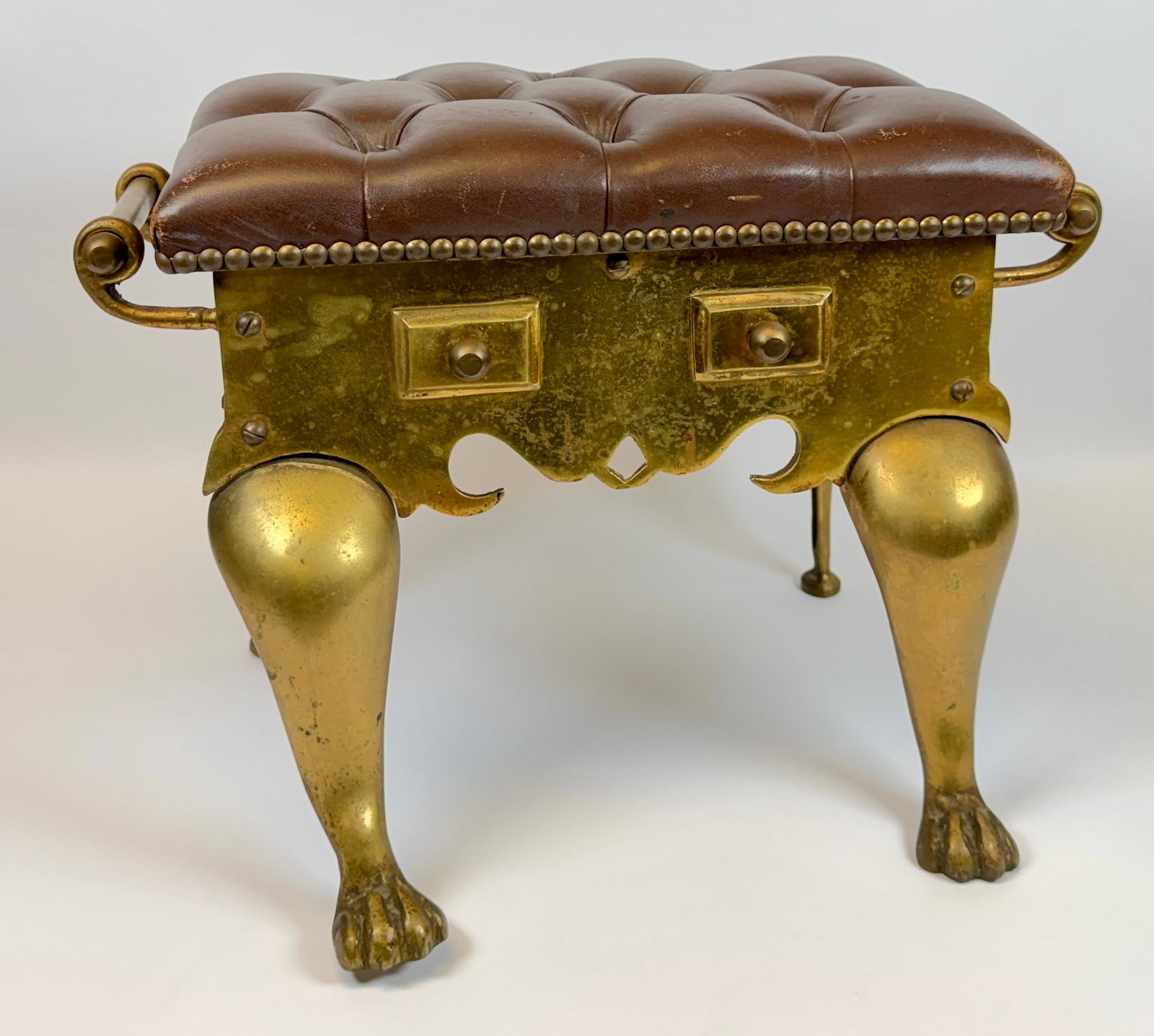 JANS OF LONDON CHESTERFIELD FOOTSTOOL: BRASS STRUCTURE WITH BROWN LEATHER TUFTED UPHOLSTERY. ONE LEG WITH REPAIR AS SHOWN. 18"X15"X14"