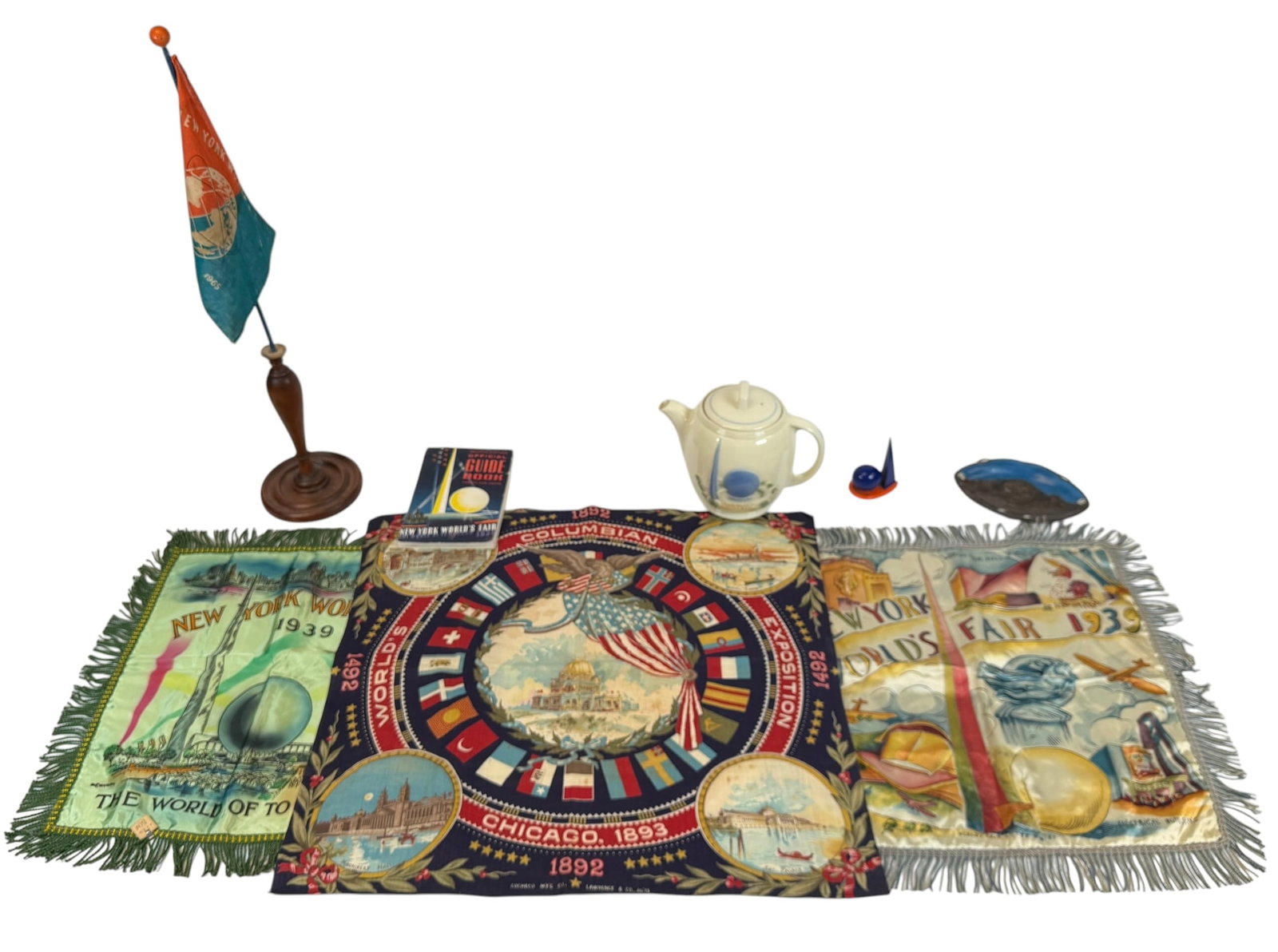 NEW YORK WORLD'S FAIR MEMORABILIA: 1965 FLAG WITH STAND, 1964/5 TRINKET TRAY UNISPHERE PRESENTED BY UNITED STATES STEEL, SALT AND PEPPER SHAKER, PORCELIER CERAMIC PITCHER, 1939 GUIDE BOOK, 1939 PILLOW COVERS (2), 1892 COLUMBIAN