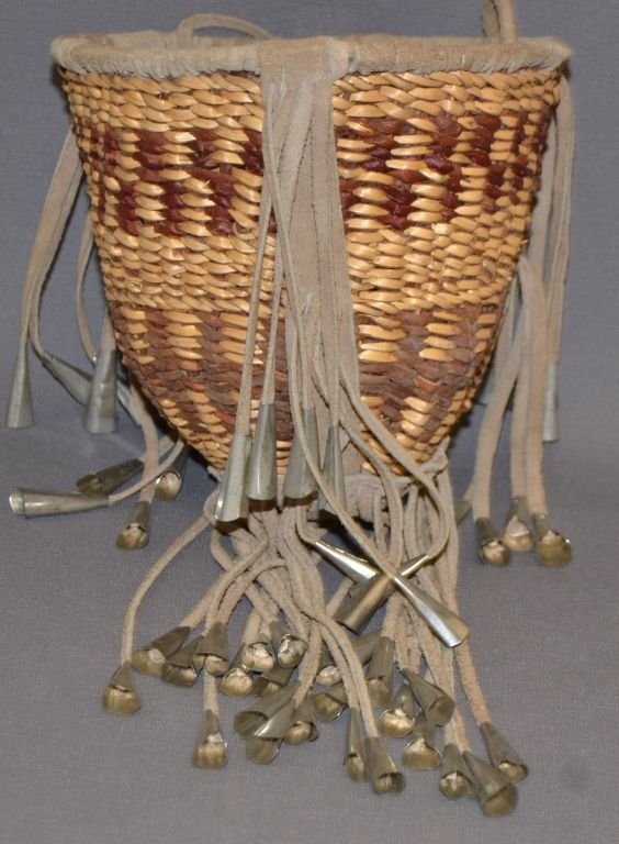 APACHE BURDEN BASKET: 1970s 80s hand woven with leather fringe and tin cones 7.5"x7.75" not including fringe Shipping charge are for the continental United States only There will be additional shipping fees on shipments to