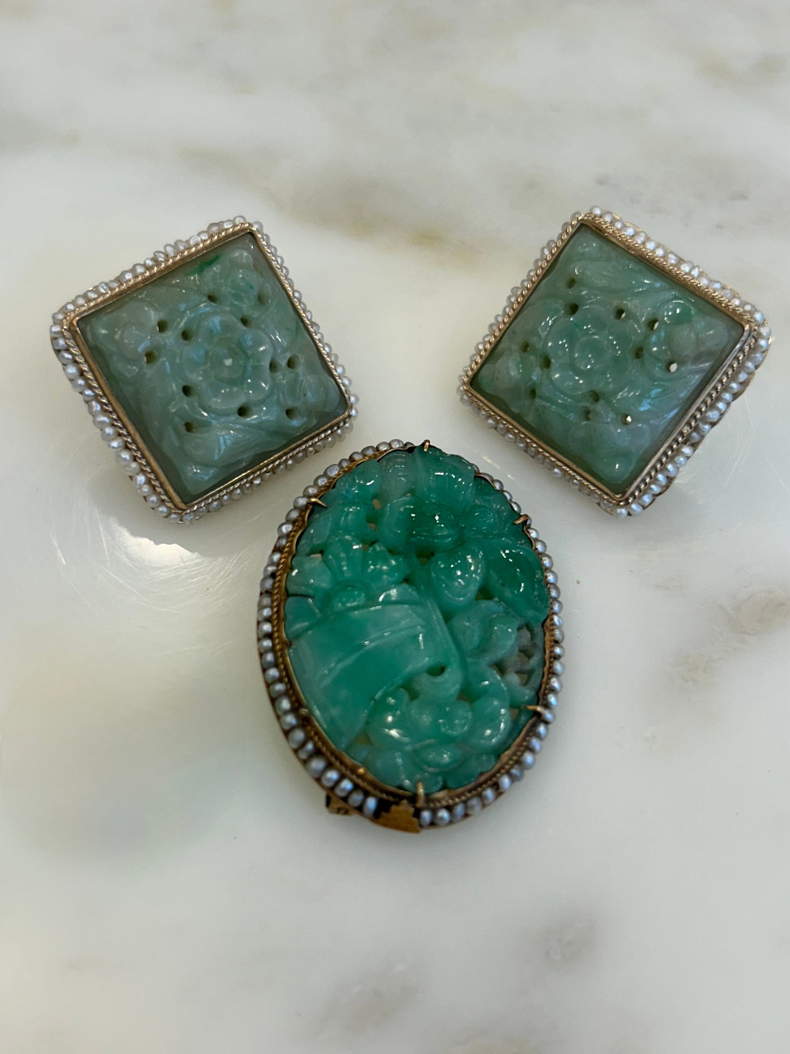 Group of Gold, Carved Jade, and Seed Pearl Jewelry: Comprising one brooch and a pair of earrings centering the oval and square carved jades, and each surrounded by small seed pearls. 14kt gold Ap. 16 dwts. (Brooch 1 1/4" h x 1 1/2" w) Crack to jade on 