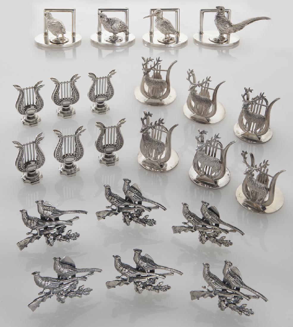 Four sets of silver place card holders;: Four sets of silver place card holders; (1) set of six lyre shaped with English hallmarks; (1) set of six with pheasants and a rifle and English hallmarks; (1) set of six with a stag standing in front