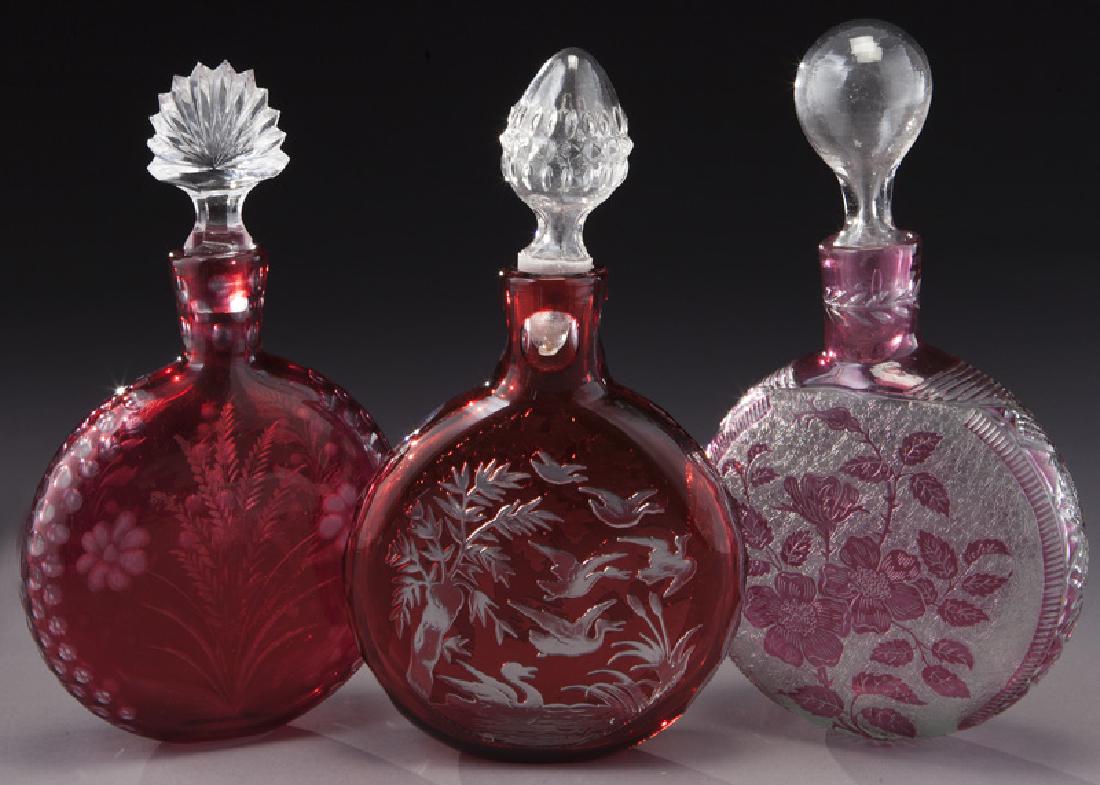 (3) Cranberry cut perfume bottles,: (3) Cranberry cut perfume bottles, including: (1) Saint Louis with cameo flowers; (1) Saint Louis with hunting scene; (1) carved with intaglio flowers. Tallest: 8.75"H, Circa - 1920. PROVENANCE: From 