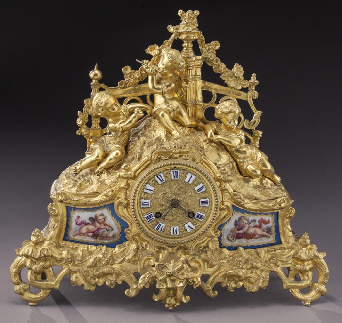 French ormolu cased mantel clock: French ormolu cased mantel clock surmounted by three cherubs and with two inset Sevres-style porcelain plaques plus porcelain hour markers. The circular brass 2-train time and bell strike movement sig