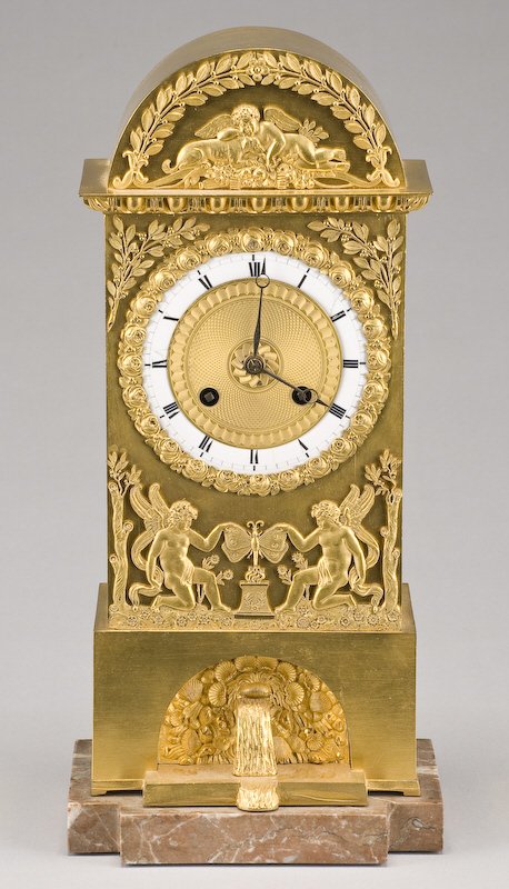 French Empire gilt bronze clock modeled: to depict the fountain of youth, on a shaped marble base. Brass eight day movement with time and bell strike with silk string suspension. With base: 13.5"H x 6.5"W x 4.5"D, Circa - Early 19th C.