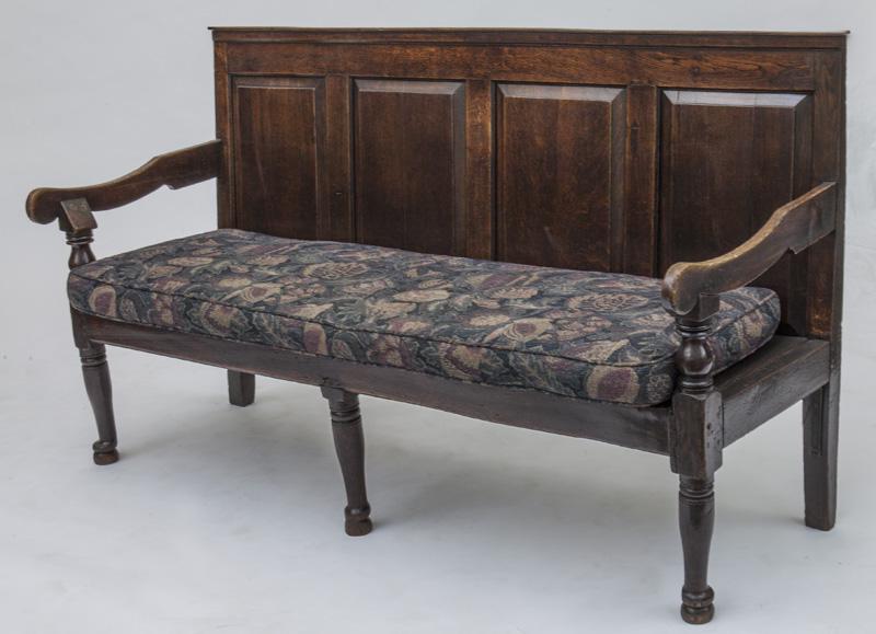 George III oak paneled back settee: of all wooden peg construction, the back with four raised panels, flat scrolled arms, on turned supports, wooden plank seat with one long cushion, on turned front legs. PROVENANCE: From the Vivian You