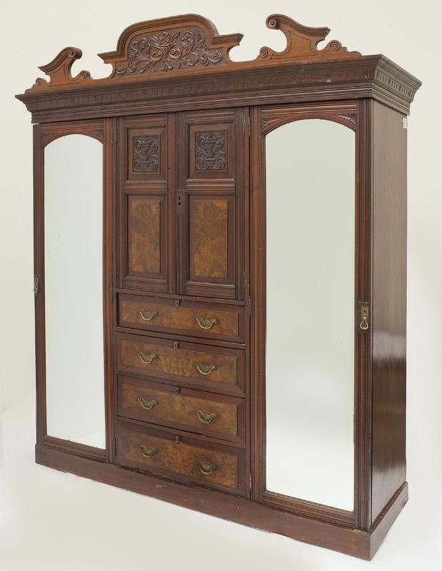 Edwardian carved and burl walnut compactum: triple wardrobe, the center section with cupboard over four drawers flanked by beveled mirror doors. PROVENANCE: From the Vivian Young and Lady Primrose's Collection, Dallas, TX. 92.5"H x 72"W x 21"D,