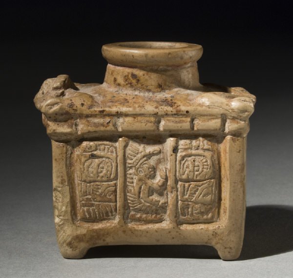 Cream slipped poison bottle of casket form surmount: Cream slipped poison bottle of casket form surmounted by an anthromorphic deity above three carved panels, lord at center, and adjacent glyph sequence. Intact and rare with mineral and manganese depos