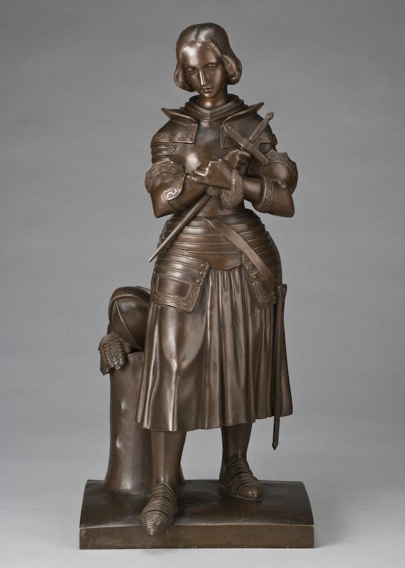 After Marie-Christine d' Orleans bronze sculpture: modeled as Joan of Arc dressed in battle attire holding a sword, having a reddish brown patina. Inscribed on side of base, "Marie D' Orleans". Marie-Christine d' Orleans (French, 1813-1839) Marie-Chri