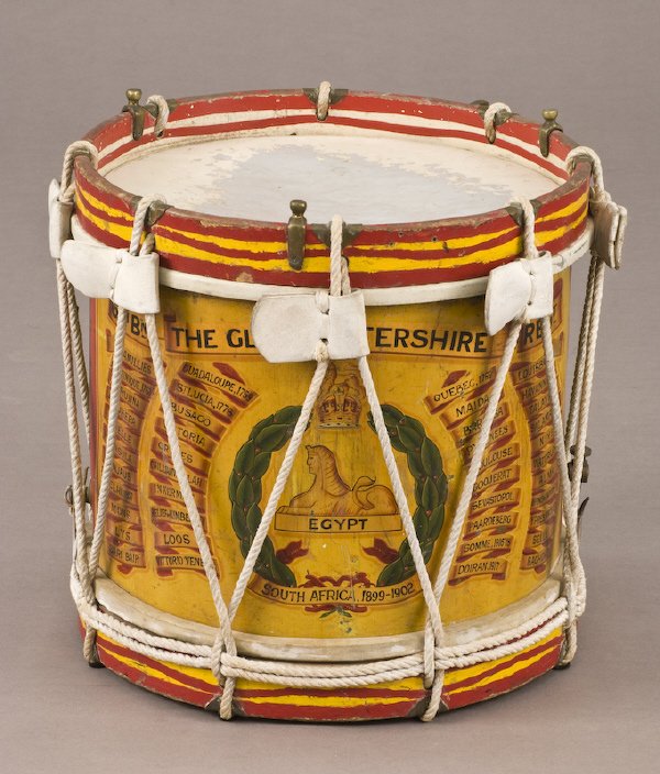 British Gloucestershire Regimental drum: The brass drum painted with Royal crest over Egyptian sphinx representing The South Africa 1899-1902 campaign surrounded, by 42 campaign battle honors. Stamped: "Henry Potter Co. London / 1933". Dress