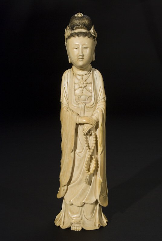 Chinese Qing carved ivory Guanyin standing,: (International shipping IS NOT available on this item. This elephant ivory was imported legally into the United States.) holding a string of beads. 11"H, Circa - 19th C.