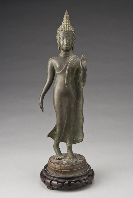 Thai bronze figure of a standing Buddha, his hands: in Buddhist mudra raised on a wood stand. 14.25"H, Circa - 19th C.