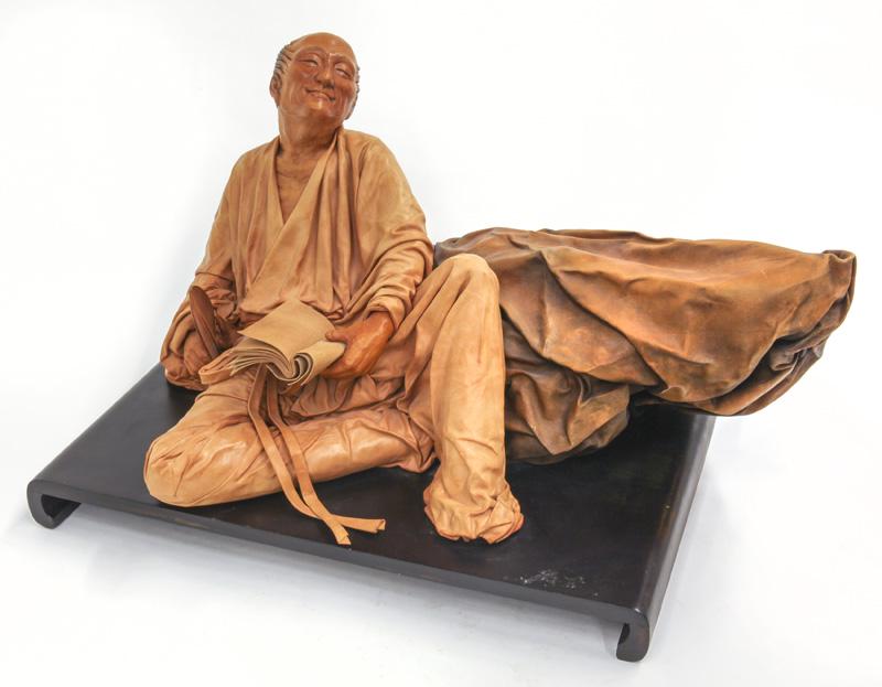 Liu Miao Chan sculpted leather figure,: Liu Miao Chan sculpted leather figure, depicting a seated man leaning against a rock and reading, raised on a wood base. Liu Miao Chan (Chinese, b. 1946). Figure: 10.5"H x 21"W x 14"D,