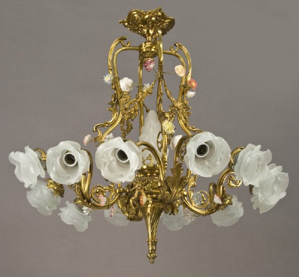 Louis XV style dore bronze chandelier: with a central frosted glass flame globe and 12 scrolled arms, the lights with flower shaped frosted glass shades. Decorated with porcelain flowers. Electrified. 30"H x 30"W, Circa - 20th C.