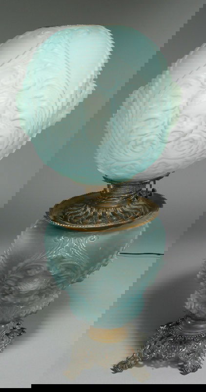 A Gone with the Wind Parlor lamp the globe and: the base both in blue satin glass with detailed cherub mask decoration, sitting of a filigree brass base. 24"H, Circa - Late 19th C.