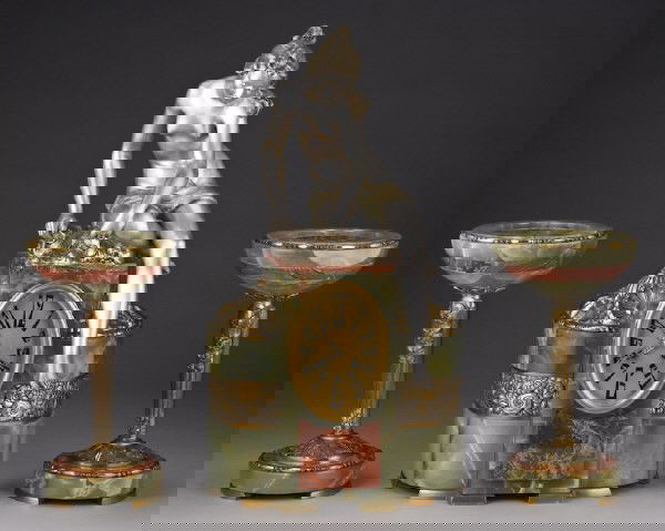 3pc. French Art Deco clock garniture set;: the clock in green onyx and marble surmounted by a silvered bronze semi-nude maiden having a circular brass 2-train bell strike movement, accompanied by a matching pair of tazzas. Clock: 22"H x 12.5"W