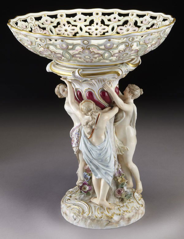 Meissen porcelain centerpiece with a reticulated: Meissen porcelain centerpiece with a reticulated basket held aloft by the three graces standing on a rocaille scrolled base. Cross swords mark in blue under glaze as well as impressed and incised mark