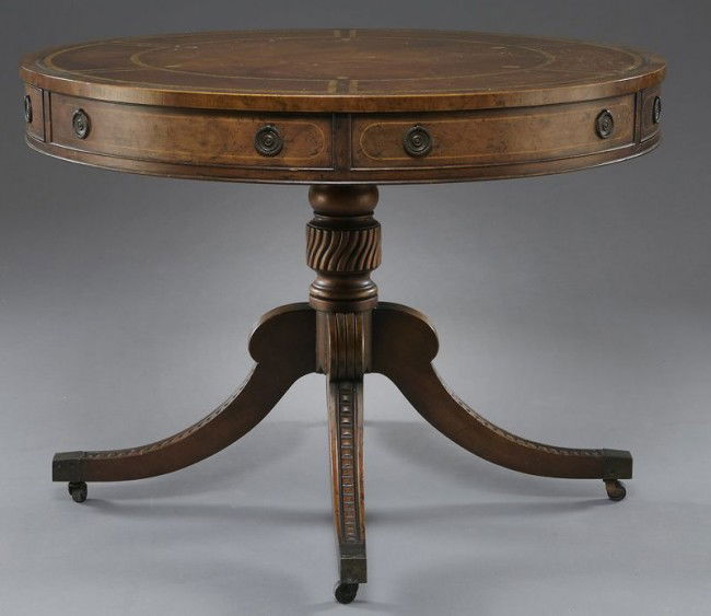 Vintage Baker mahogany drum table: the round top inset with distressed gold tooled leather skiver over two curved front drawers and two sham, raised on a turned standard with four carved down swept legs terminating in brass casters. Dr