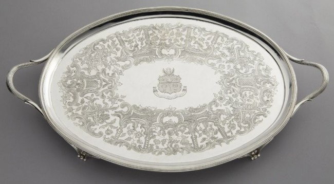George III sterling oval footed tray by John Wren: with reeded handles as well as a reeded rim centering ornate engraved borders around a central crest and motto that reads, "Nobilitas Sola Virtus"; the whole raised on tapering scrolled feet. Marked f