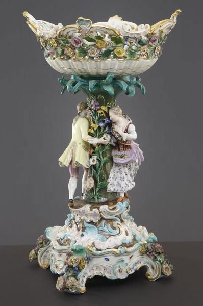 Meissen porcelain figural centerpiece on stand,: the reticulated compote raised on a flower encrusted standard, flanked by a lady pursued by her gallant, on a scrolled rocaille base. Crossed swords mark in blue under glaze, incised "2772" on compote