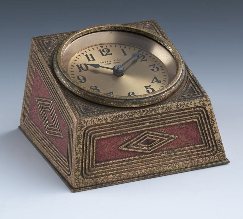 Tiffany Studios gilt bronze desk clock with: geometric decoration. Dial marked, "Tiffany and Co. New York". Signed, "Tiffany Studios New York 1816". 2.75''H x 4''W x 4.25''D, Circa - 1930.