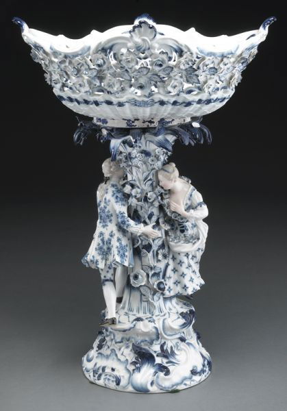 Meissen porcelain figural compote in "Blue Onion": pattern, the reticulated bowl raised on a tree-form standard, flanked by a maiden pursued by her suitor, raised on a plinth. Cross swords mark in blue under glaze, as well as impressed numerals. 19.5'