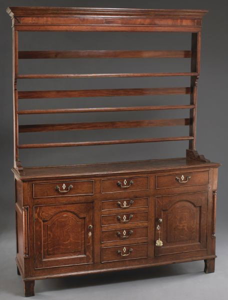 George III oak Welsh dresser: George III oak Welsh dresser of two part construction, the molded cornice above a mahogany veneered frieze and three open plate racks, the lower cabinet with three frieze drawers over four central dra
