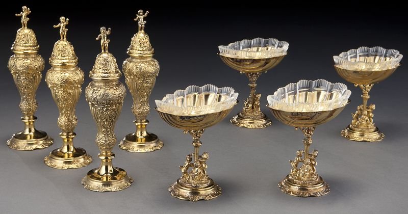 8 Pcs. German 800 silver vermeil tableware, incl.:: 8 Pcs. German 800 silver vermeil tableware, incl.: (4) salt cellars of shell form raised above putti playing with birds, each bowl fitted with a glass insert, 3.75''H without glass; and (4) shakers de