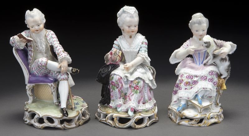 (3) Meissen porcelain figures applied with lace,: (3) Meissen porcelain figures applied with lace, including: (1) gentleman seated reading a book; (1) seated lady feeding her cat; and (1) seated lady holding a black cloak. All raised on pierced rocai