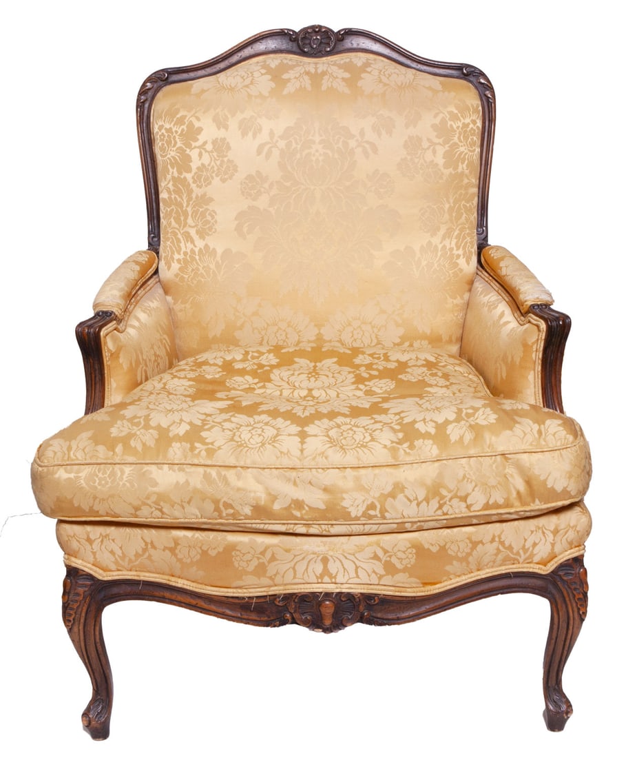 Upholstered Wooden French Style Armchair: Carved wood details on the top and legs. Upholstered yellow satin with floral pattern. Some damage to the arms. Measuring H 37 W 30 D 29 in
