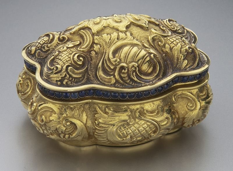 22K gold and sapphire snuff box: 22K gold and sapphire snuff box with repousse scrolls and shells in high relief, mounted with 63 Ceylon sapphires, 5.0 cts. approximate total. Stamped, "*A" and bearing a fleur de lis shaped mark. Tes