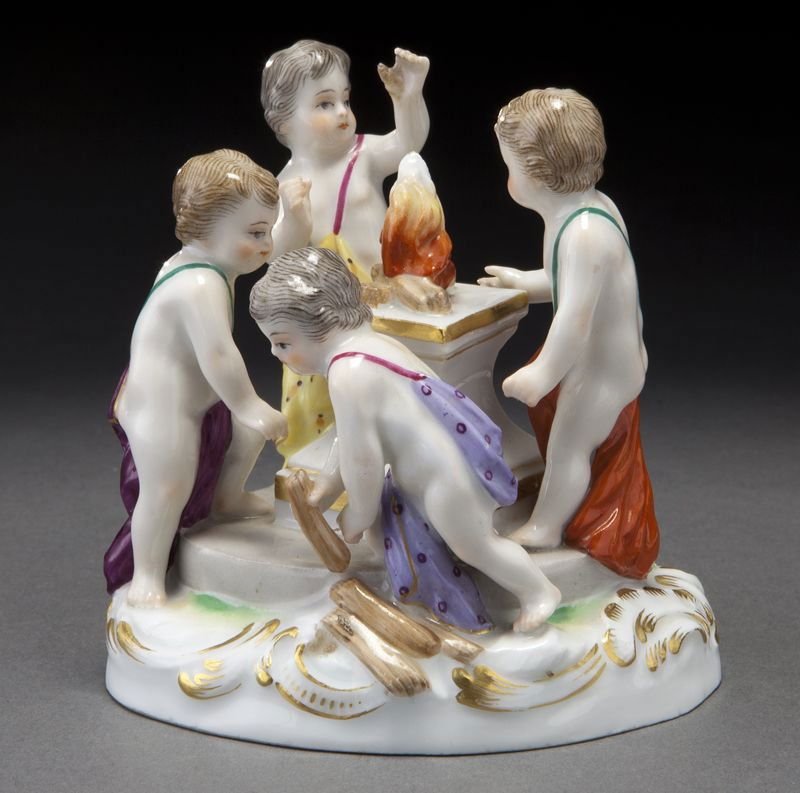 Meissen porcelain figural group of four putti: Meissen porcelain figural group of four putti around a fire burning on a plinth, on an oval gilt decorated base. Cross swords mark in blue under glaze, as well as impressed and incised numerals. 3.5''